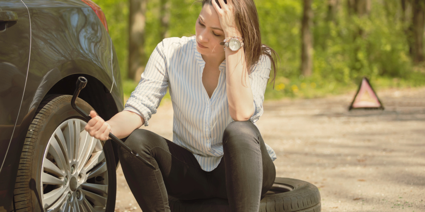 mulher sentada na rua com cara preocupada olhando para o pneu furado